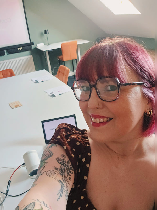 Person with pink hair and glasses in an office setting